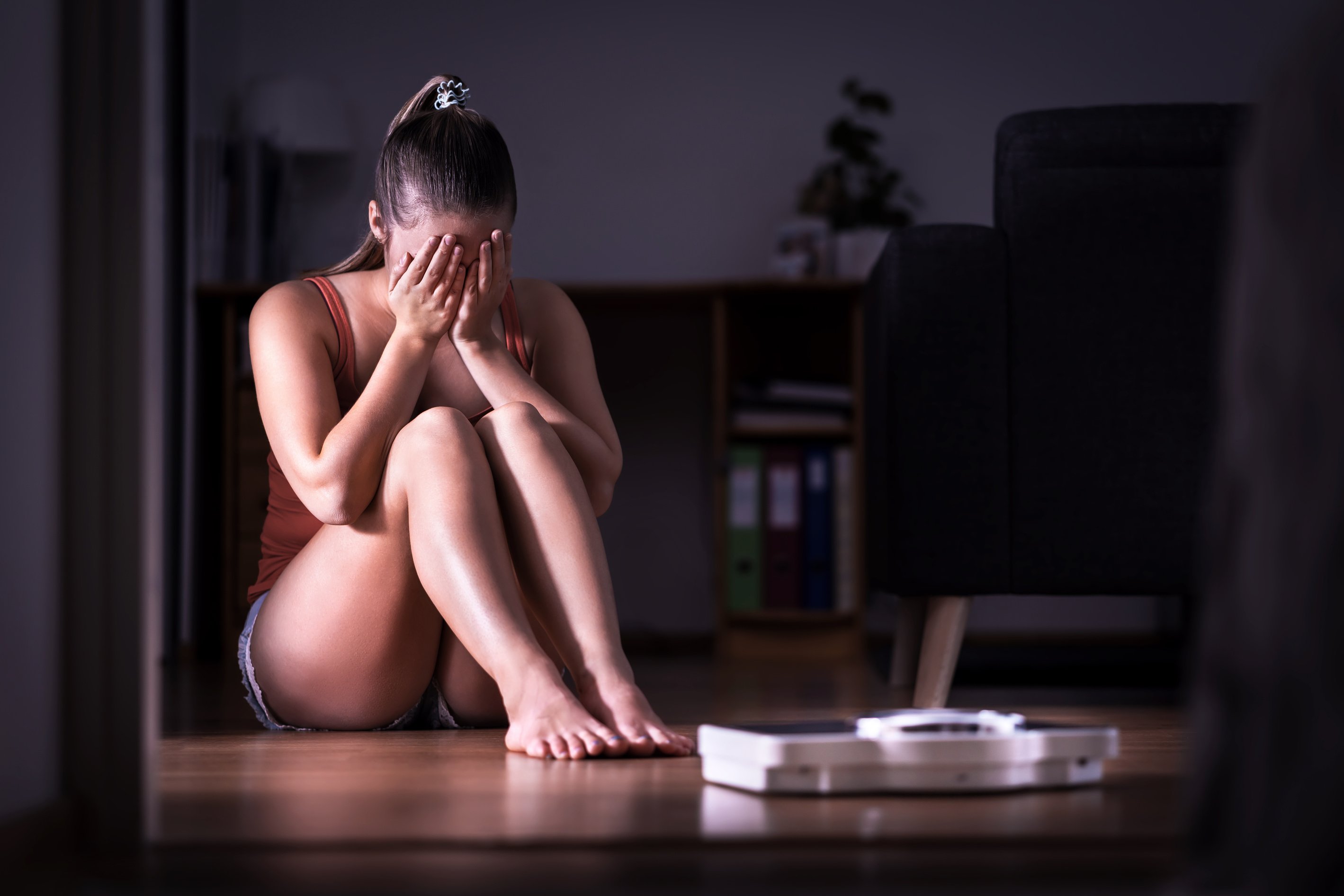 Woman having stress about weight loss, diet or gaining weight. Eating disorder, anorexia or bulimia concept. Young girl crying and sitting on the floor with scale.